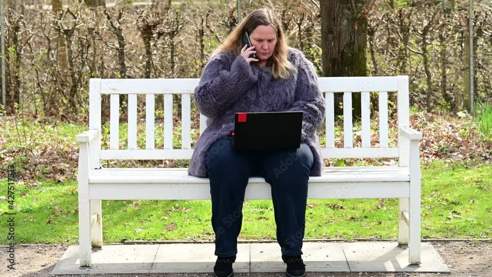 Frau in einer Kaninchenfell Jacke arbeitet im Garten mit einem Notebook im Homeoffice Frau in einer Kaninchenfell Jacke arbeitet im Garten mit einem Notebook im Homeoffice