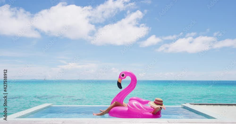 Travel vacation holidays concept. Woman in pool by beach sunbathing in bikini in inflatable pink flamingo toy mattress float in. Girl relaxing enjoying luxury lifestyle at resort pool.