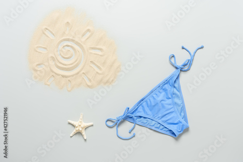 Beach blue bikini on a pastel grey background. Female sexy colored bikini bottoms or panties. Drawing of the sun on the sand and a starfish. Summer vacation concept. Top view  flat lay  copy space