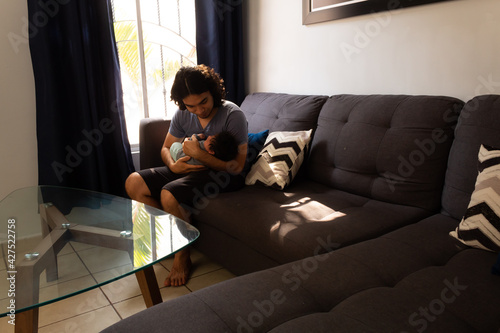 young happy hispanic father hugging and holding his newborn baby