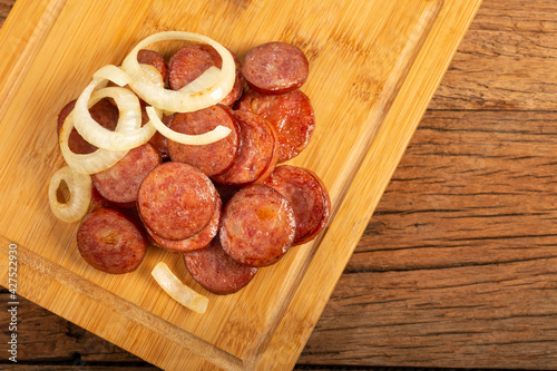 Sliced ​​calabrese sausage with onion on wooden background. photo