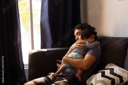 young happy hispanic father hugging and holding his newborn baby