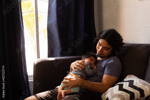 young happy hispanic father hugging and holding his newborn baby