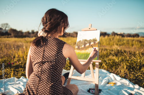 Giovane ragazza italiana dipinge il quadro in un prato di pomeriggio photo