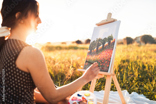 Giovane bella ragazza dipinge il quadro su tela seduta su un prato in campagna