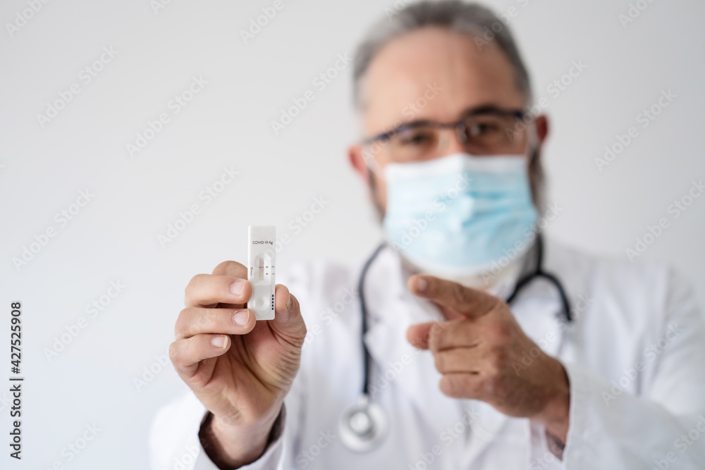 Portrait of a blurred senior doctor in face mask showing Covid-19 PCR result. Portrait of a blurred senior doctor in face mask showing Covid-19 PCR result.