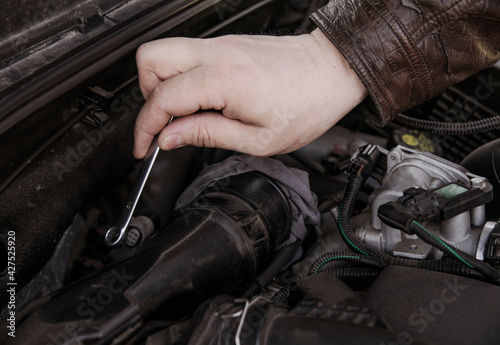 A man unscrews the nuts at the EGR valve in the hood of the car with a screwdriver