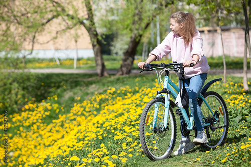 Teenager girl riding bicycle in spring park with yellow flowers