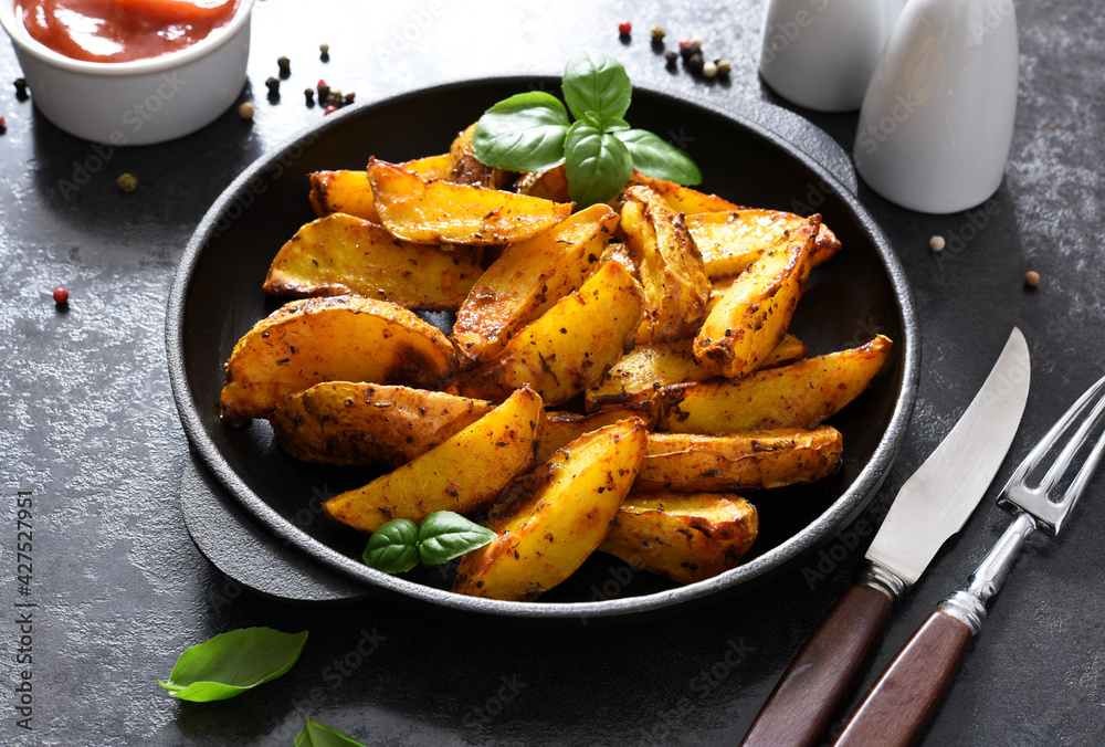 Fried potato wedges in a frying pan and sauce on a concrete background. Baked potato slices. Fried potato wedges in a frying pan and sauce on a concrete background. Baked potato slices.