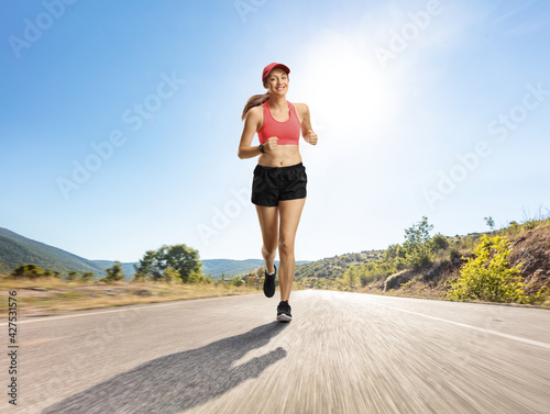 Female jogger in shorts running on an asphalt road