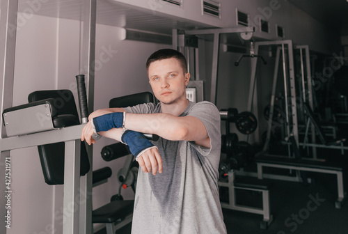 a portrait of a tired athlete in a wet T-shirt stands near the simulator.