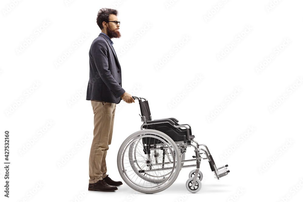 Full length profile shot of a bearded man pushing an empty wheelchair Full length profile shot of a bearded man pushing an empty wheelchair