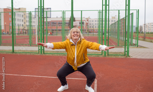 an elderly woman in a yellow jacket is doing sports exercises on a red treadmill. the stadium is a healthy lifestyle. retired people and sports.