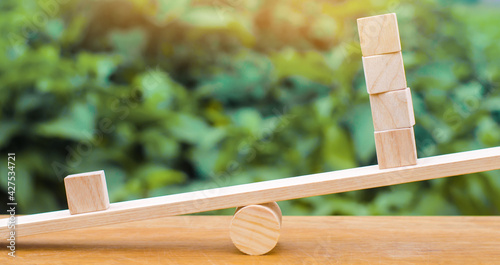 One wooden block on the scales outweighs the other four. Inequality concept. One against the others. Leadership and uniqueness. Unique, dissenting opinion, individual and standing out from the crowd photo