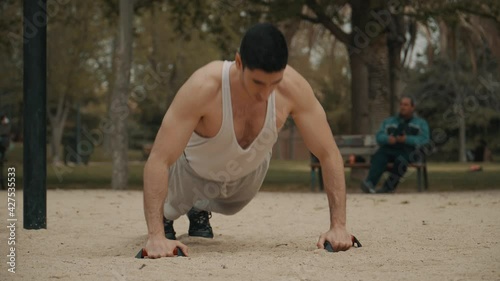 hombre haciendo flexiones en el parque, hombre de pelo negro haciendo deporte al aire libre, hombre musculoso en camiseta de tirantes  blanca haciendo ejercicio photo