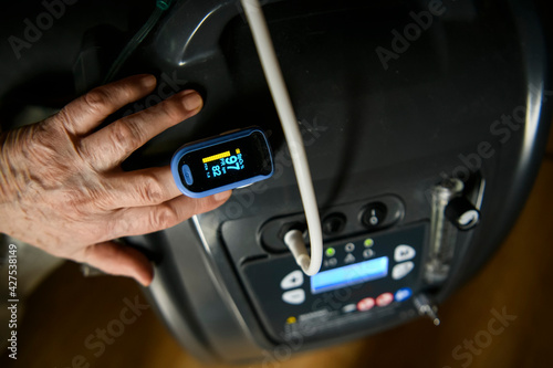 View of a hand of a woman with an pulse oximeter clipped on the index finger. Hand lies on a medical oxygen concentrator