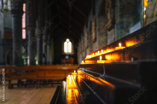 Selective focus on votive lit candle with bright soft glow and blurred background of interior of St. Marys Cathedral in Killarney, Kerry, Ireland photo