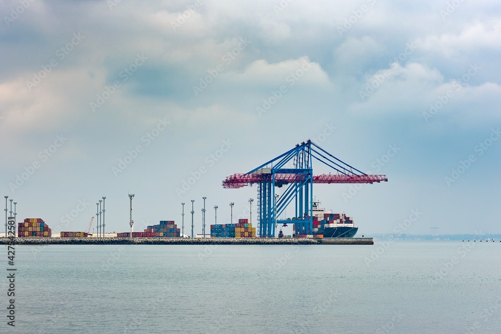 Port cargo crane loads a container onto a cargo ship in a seaport on a cloudy day Port cargo crane loads a container onto a cargo ship in a seaport on a cloudy day