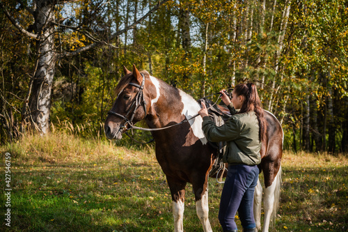 A young girl tied a beautiful horse to a fence on a ranch to ride it