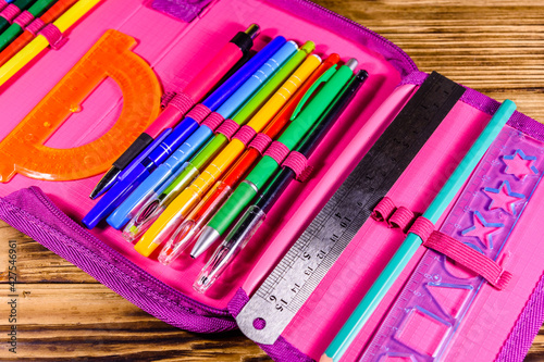 Different school stationeries (pens, pencils, ruler and protractor) in a pink pencil box