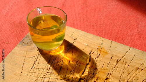 Fully linden tea filled glass pot existing on wooden plate and red carpet. Isolated linden tea cup made of glass and there is green mentholated sweat and candy.  photo