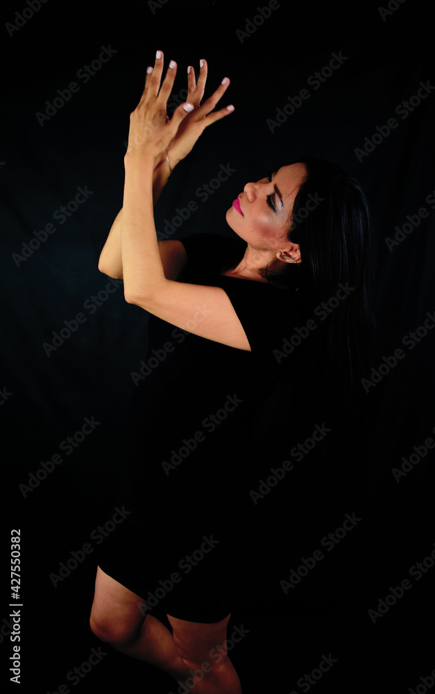Mujer latina muy elegante mirándose las manos con vestido negro en una estudio fotográfico Mujer latina muy elegante mirándose las manos con vestido negro en una estudio fotográfico