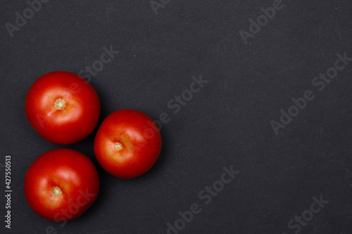 Zbliżenie na trzy czerwone dojrzałe pomidory na czarnym tle, miejsce na tekst