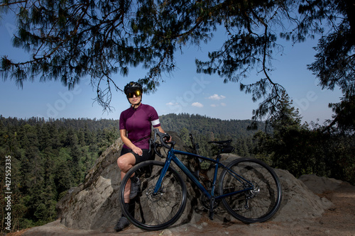 mujer latina con bicicleta descansando en el bosque, con un paisaje de arboles al fondo. Concepto deporte al aire libre