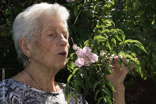 old lady smelling a pink flower in the garden of her house