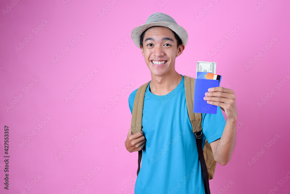 Young Asian tourist man holding credit card, money, and saving book, wears casual cloth, backpack, and hat Young Asian tourist man holding credit card, money, and saving book, wears casual cloth, backpack, and hat