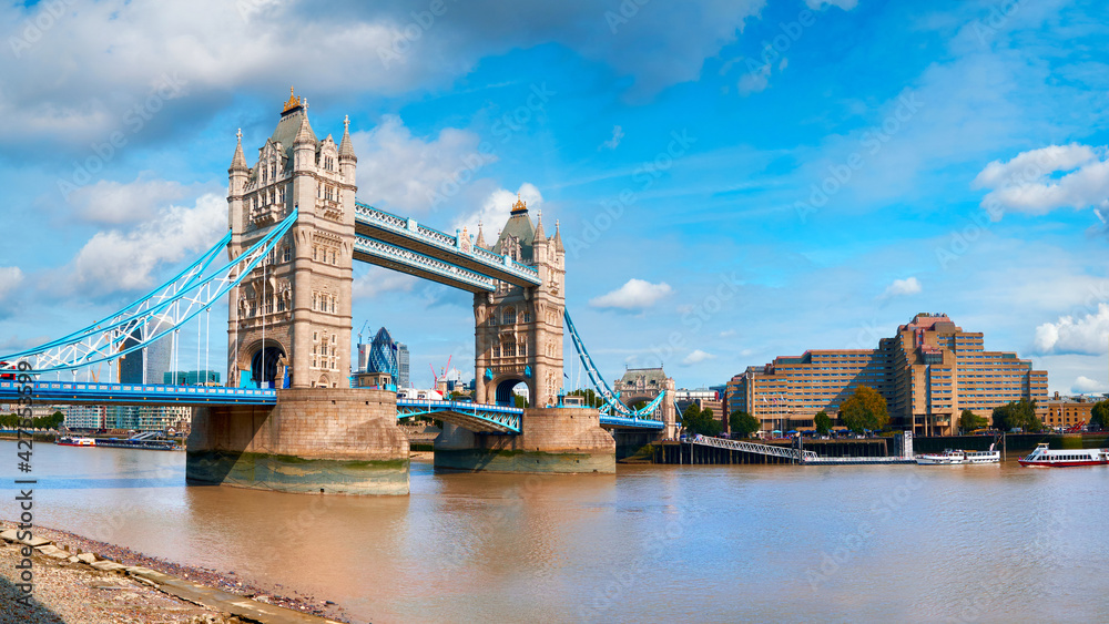 Fototapeta premium Tower Bridge on a bright sunny day with blue sky and clouds. Calm water with reflections. London, England, UK.