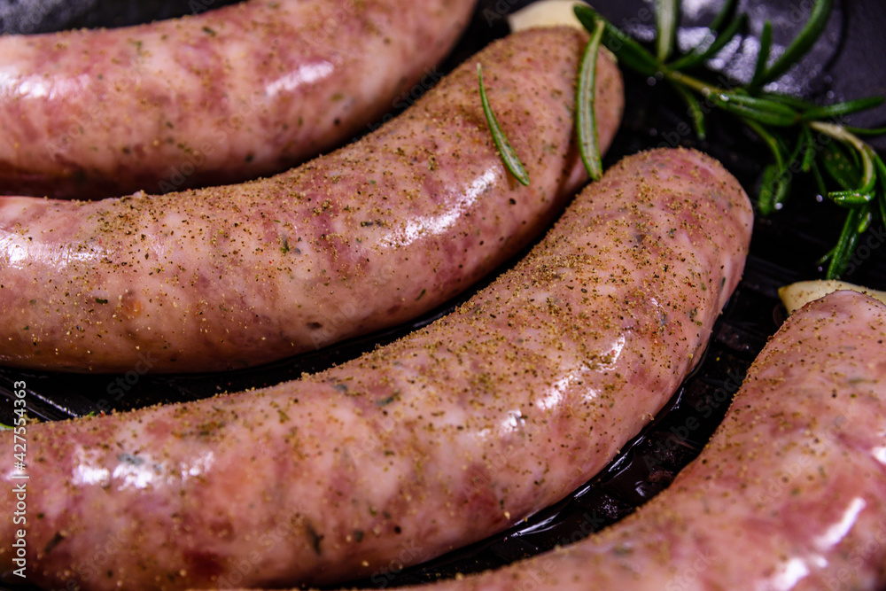 Raw sausages with rosemary twigs and garlic in a cast iron grill pan Raw sausages with rosemary twigs and garlic in a cast iron grill pan