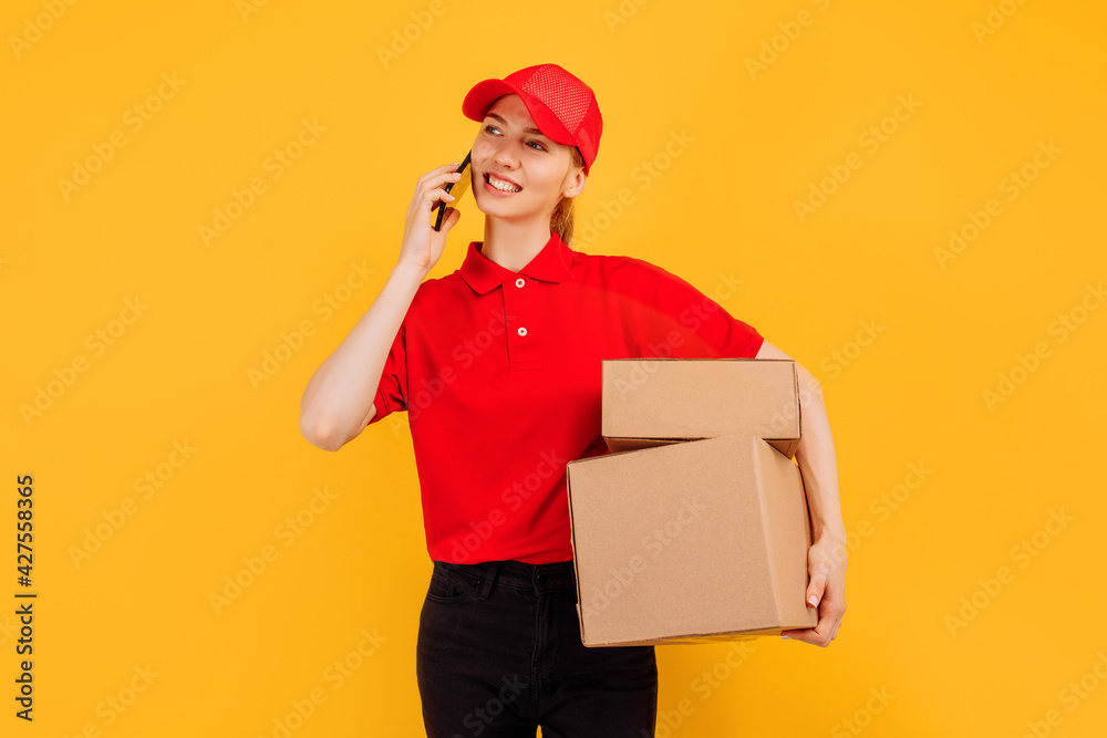 Delivery service worker holding a cardboard box and talking on a cell phone, on a yellow background