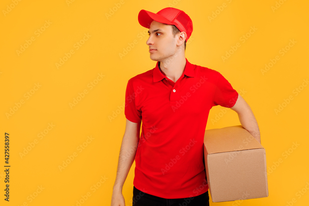 happy young courier in red hat standing with mailbox isolated on yellow background
