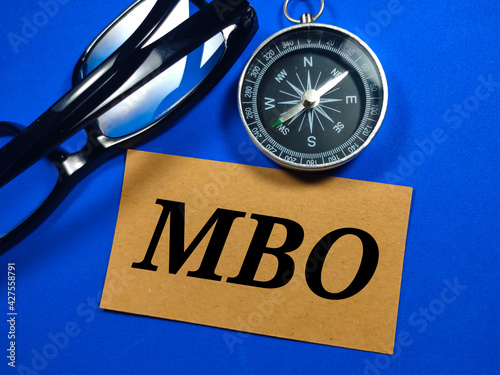 Selective focus of compass and eye glasses with word MBO (Management By Objectives) on blue background.Business concept.