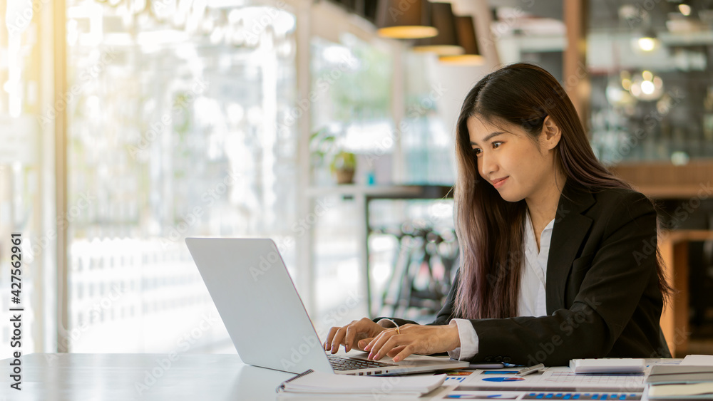 A business woman working in an office sitting at a business statistical chart analysis desk holding a chart using a laptop A business woman working in an office sitting at a business statistical chart analysis desk holding a chart using a laptop