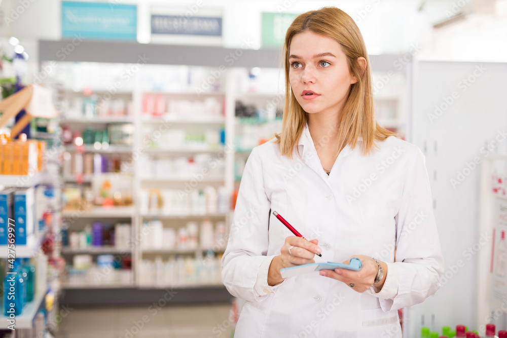 Smiling female pharmacist checking assortment of drugs in pharmacy