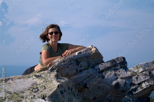 Smiling woman resting on top of cliff after climbing © Max