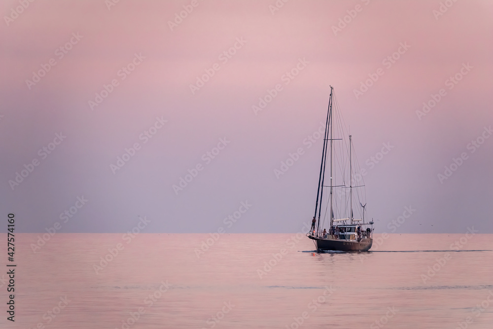 Fototapeta premium Sailing yacht in the blue sea during beautiful pink sunset.