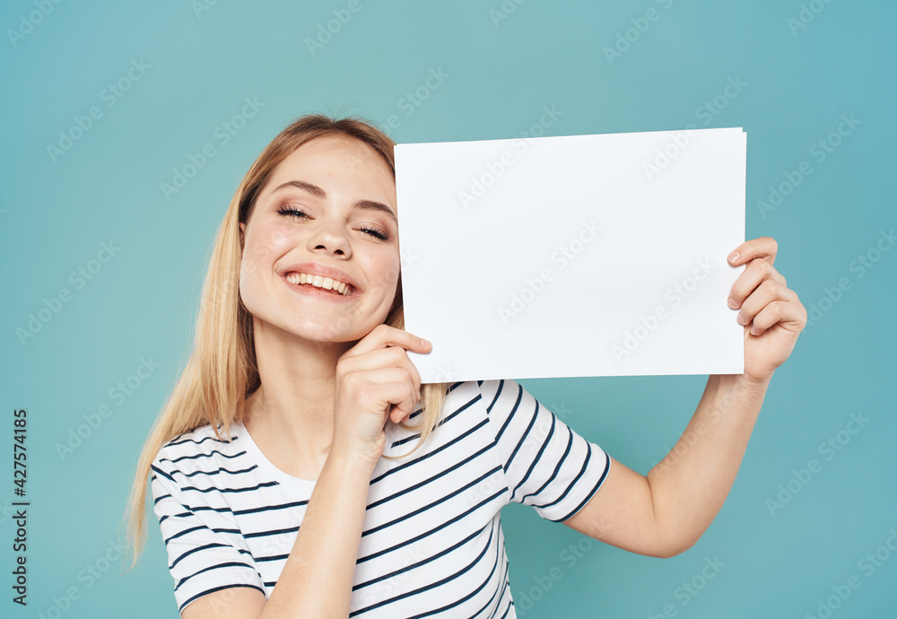 Beautiful blonde on a blue background with a white sheet of paper banner advertising positive gesture Beautiful blonde on a blue background with a white sheet of paper banner advertising positive gesture