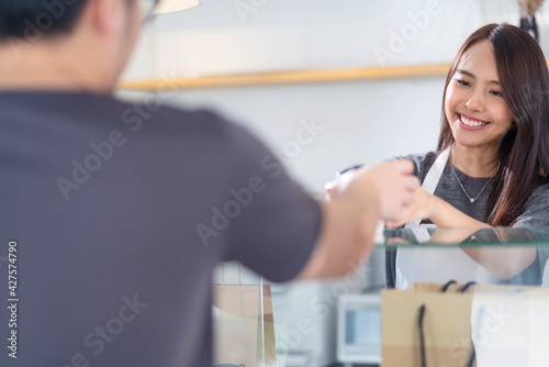 Attractive asian female cafe worker  giving takeaway food bag coffee cup to customer. Coffee shop worker offering takeout safe restaurant take away delivery