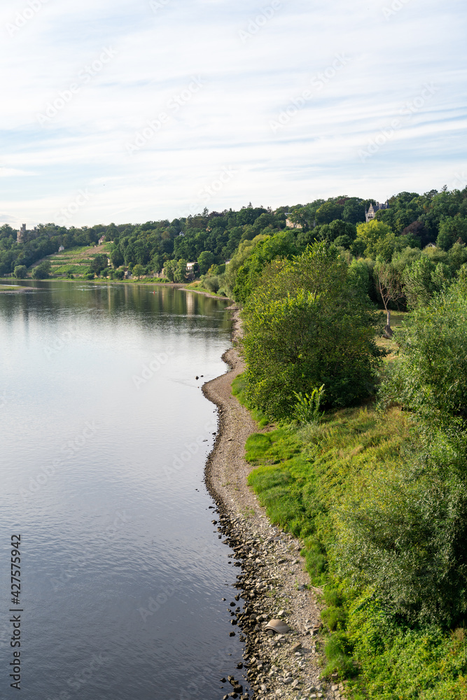 Fototapeta premium A beautiful view on the horizon of the green hills with villas, the calm river and a lawn with a path in the city of Dresden on a summer day. Travel and nature concept