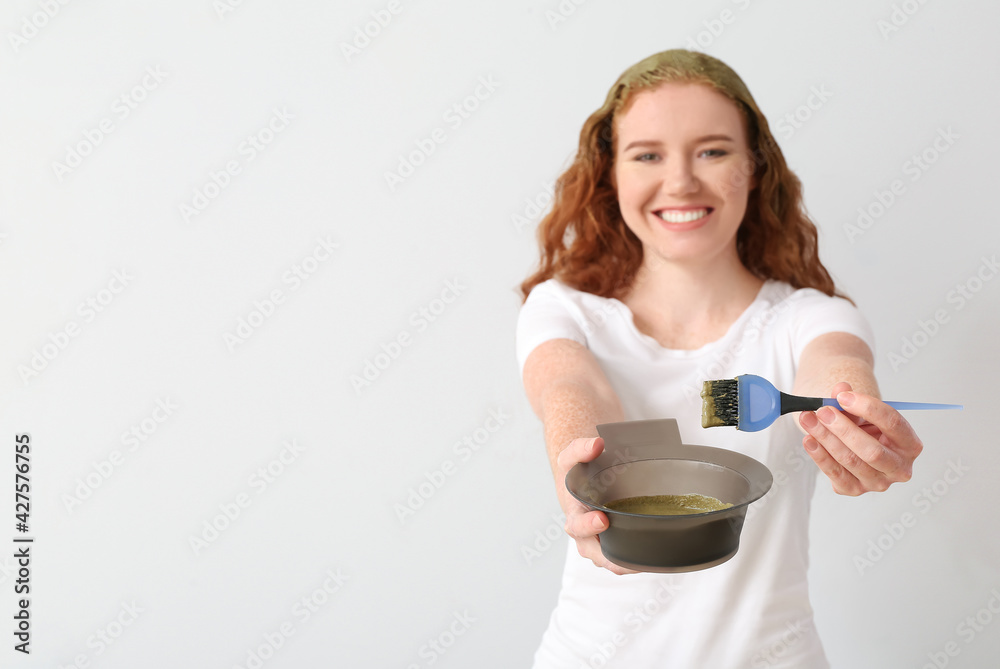 Young woman using henna hair dye on light background Young woman using henna hair dye on light background