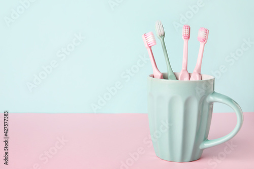 Cup with tooth brushes on color background