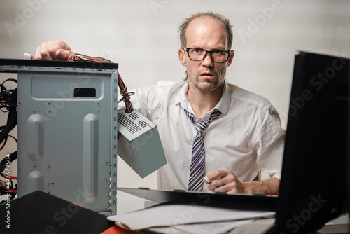 Portrait of desperate office worker trying to fix broken computer photo