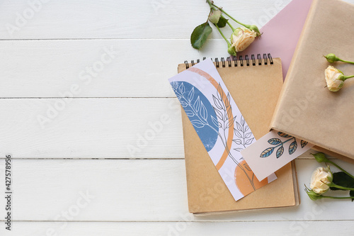 Book, notebook, bookmarks and flowers on light background