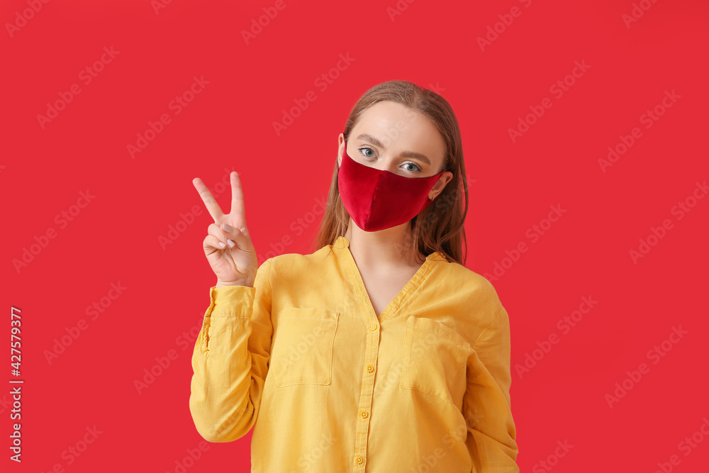 Stylish young woman wearing mask and showing victory gesture on color background Stylish young woman wearing mask and showing victory gesture on color background