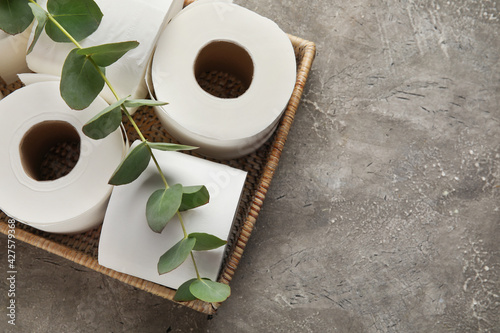 Basket with rolls of toilet paper and eucalyptus branch on grunge background photo