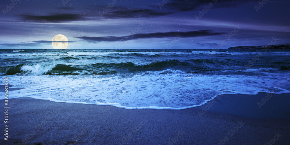 sea tide on a cloudy sunrise. green waves crashing golden sandy beach in full moon light. storm weather approaching. summer holiday concept