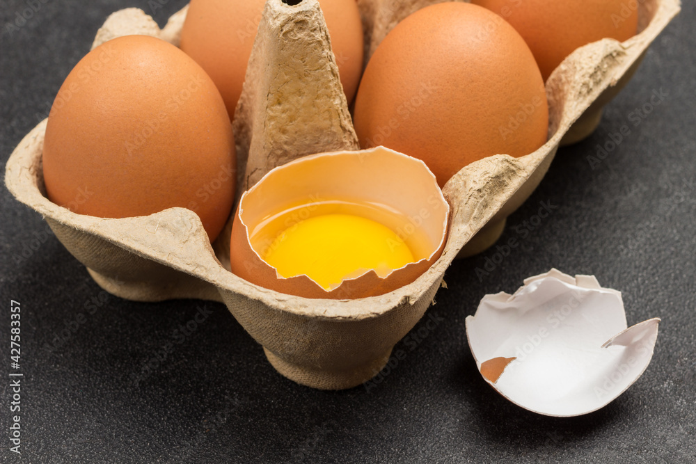 Brown chicken eggs in carton container. Broken egg in container. Shells on table Brown chicken eggs in carton container. Broken egg in container. Shells on table